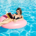 Beautiful crazy woman reading a book on inflatable ring in blue swimming pool.