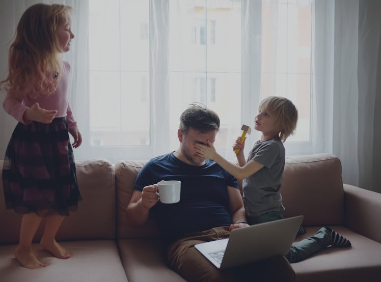 Tired father with his two kids at home, as he tries to work on a laptop on a couch.