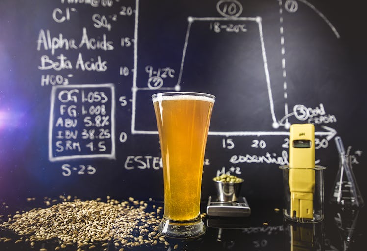 A big glass full of beer placed on a black desk in front of a blackboard filled with formulas