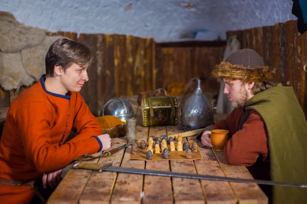 Two men in russian ethnic suit playing medieval popular strategy board game - tafl. Folk, competitio...