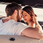 Romantic couple is sitting in green retro car on the beach. Handsome bearded man and attractive youn...