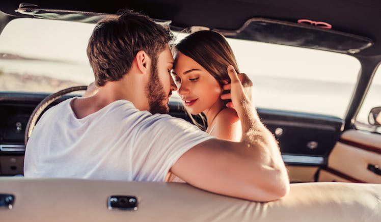 Romantic couple is sitting in green retro car on the beach. Handsome bearded man and attractive youn...