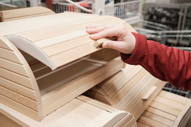 Girl in a store buys a wooden container for storing bread and food. The concept of buying new dishes...