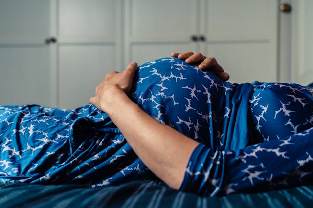 A pregnant woman wearing a night gown is lying on a bed with her hand on her belly