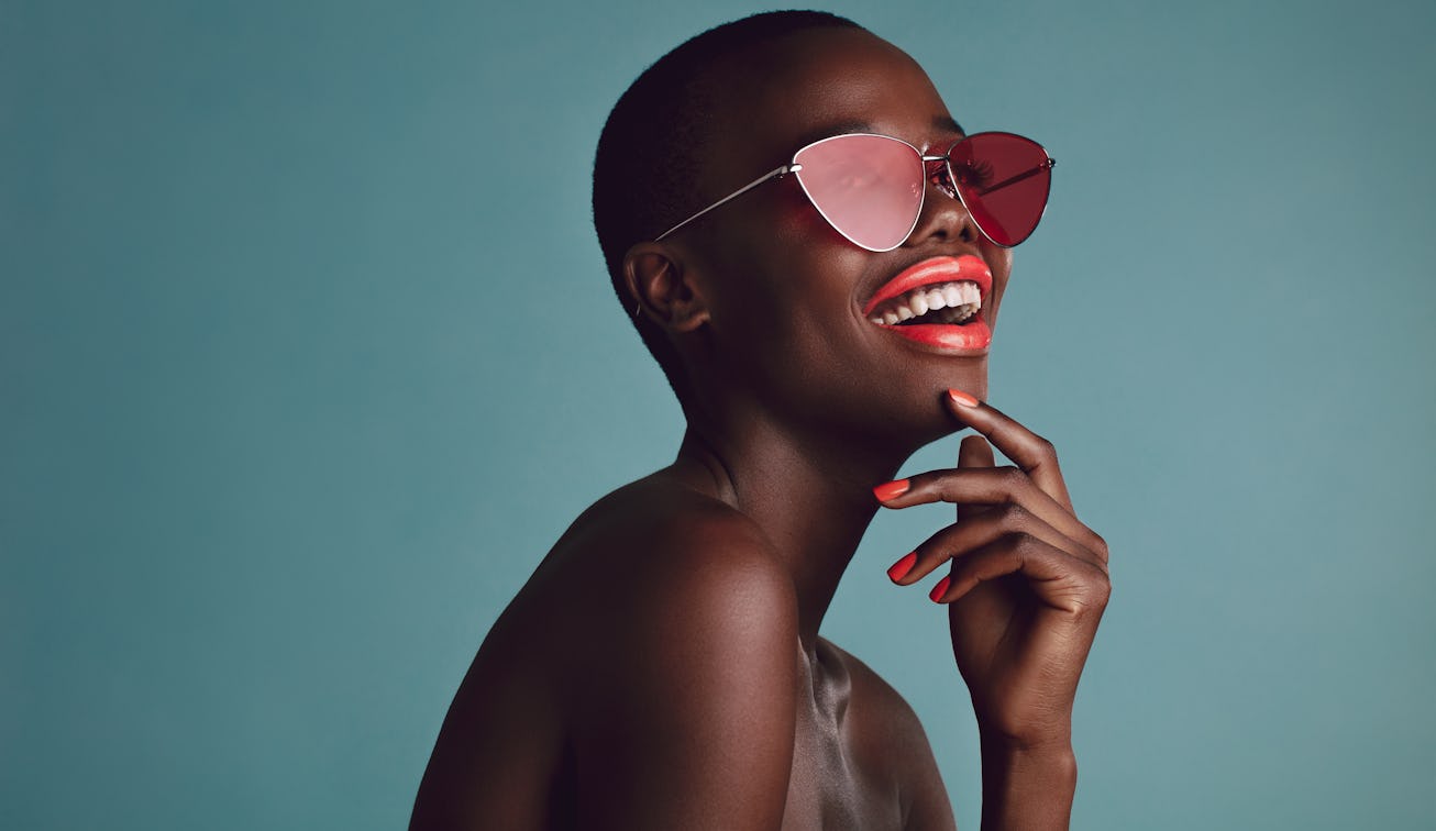 Close up shot of beautiful woman in sunglasses and red lips against grey background. African female ...