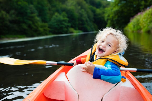 Happy kid enjoying kayak ride on beautiful river. Little curly toddler boy kayaking on hot summer da...