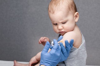 Pediatrician or nurse giving an intramuscular injection of a vaccine to arm of a baby girl during co...