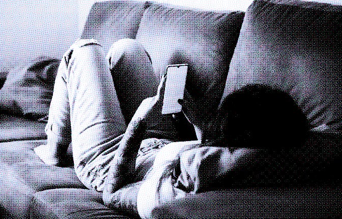 Young redhead girl with freckles looking at her smartphone on the sofa in her living room, relaxed, ...