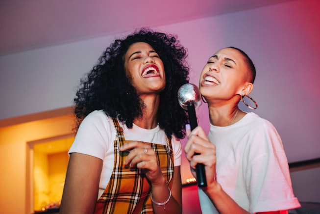 Best friends singing into a microphone on karaoke night. Two cheerful young women singing their favo...