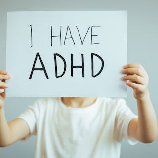 Young boy holds ADHD text written on sheet of paper. ADHD is Attention deficit hyperactivity disorde...