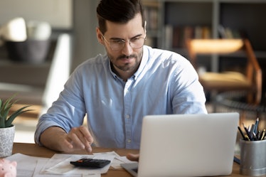 Focused young Caucasian man look at laptop screen calculate expenses expenditures pay bills taxes on...