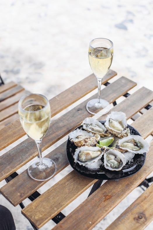 Two glasses of wine wine and a plate with oysters and limes on a wooden table. Outdoors, sunny weath...
