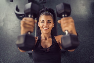 Concentrated woman lifting dumbbells in gym