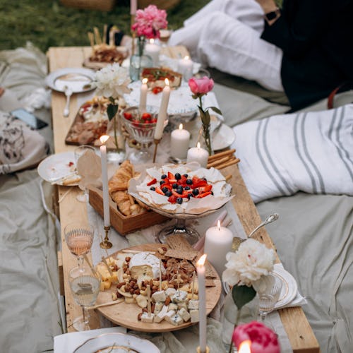outdoor picnic feast. festive pallet table with desserts and snacks. people sitting near the table w...