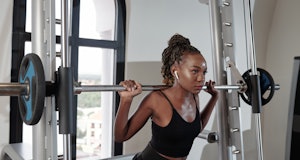 Serious concentrated young sportswoman listening to music in earbuds when lifting barbell