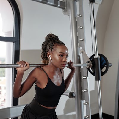 Serious concentrated young sportswoman listening to music in earbuds when lifting barbell