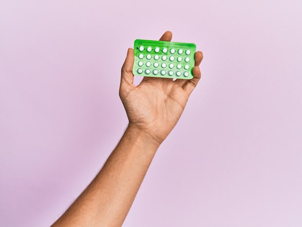 Young hispanic hand holding birth control pills over isolated pink background.