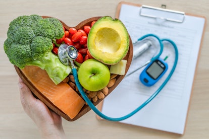 Vegetables in a wooden heart-shaped basket with a stethoscope coping out of it, beside medical paper...