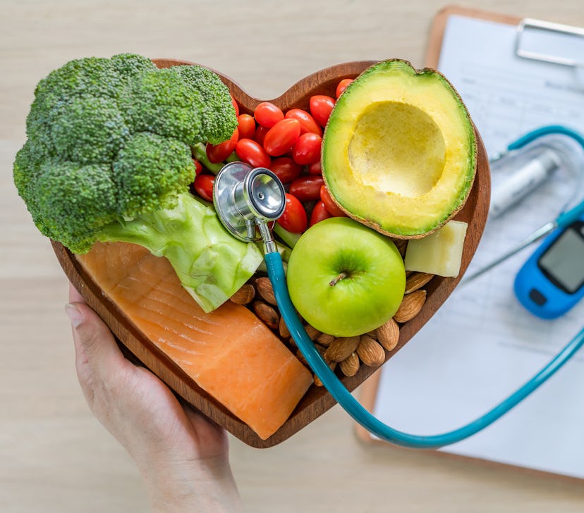 Vegetables in a wooden heart-shaped basket with a stethoscope coping out of it, beside medical paper...