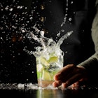 Cocktail splash with ice cubes and lime. Preparing of the delicious fresh cocktail on the bar stand