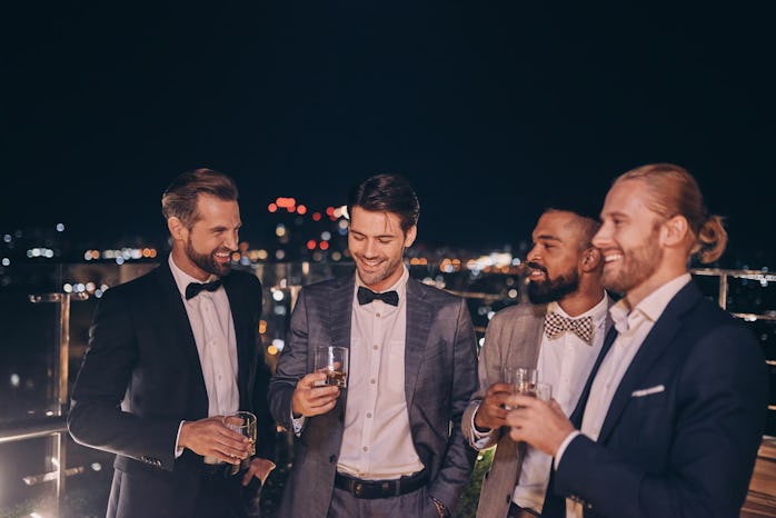 Group of handsome young men in suits and bowties drinking whiskey and smiling