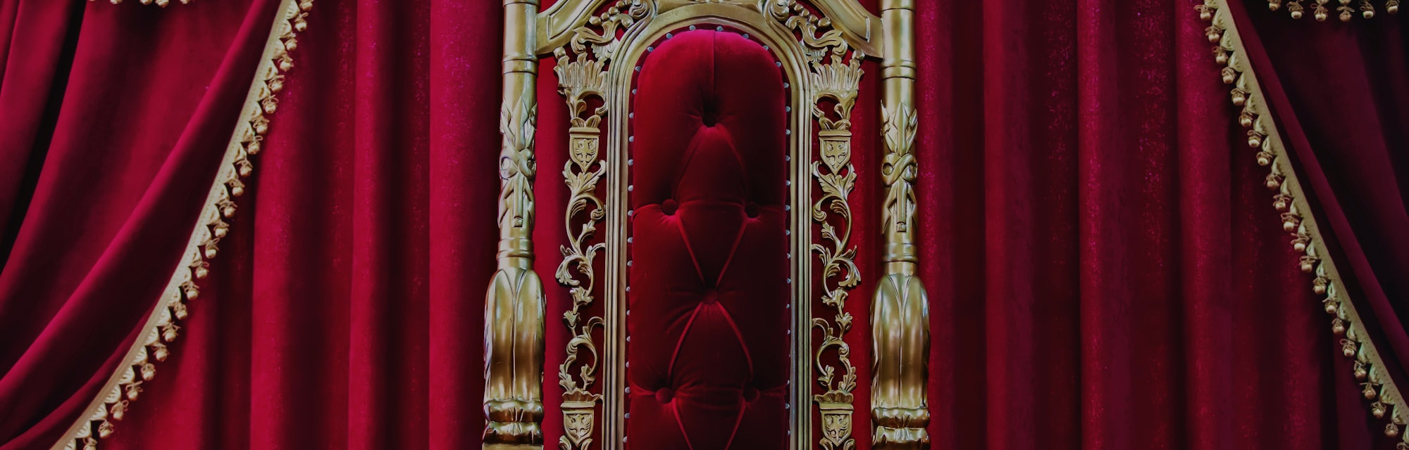 Part of the red royal chair against the background of red curtains. A place for a king. Throne