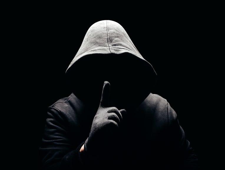 Photo of a scary horror man in hoodie showing silence hand sign in dark.