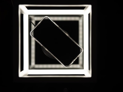 Mobile phone on wireless charger, black background with led lighting and reflections on the glass su...