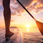 Stand up paddle boarding or standup paddleboarding on quiet sea at sunset with beautiful colors duri...