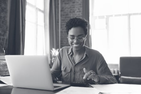 A Black woman in glasses sits at her desk, smiling.