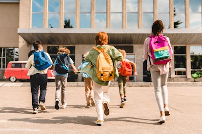 Little kids with backpacks running into school