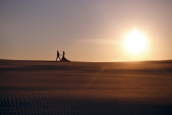 bride and groom walk in the desert during sunset, the silhouette of a man and woman, a man leads a g...