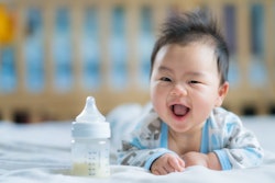Asian baby smiles with a bottle of formula