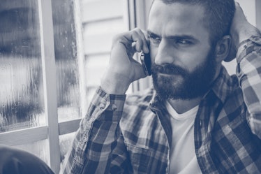 Depressed young bearded man expressing negativity while talking on the mobile phone and looking thro...