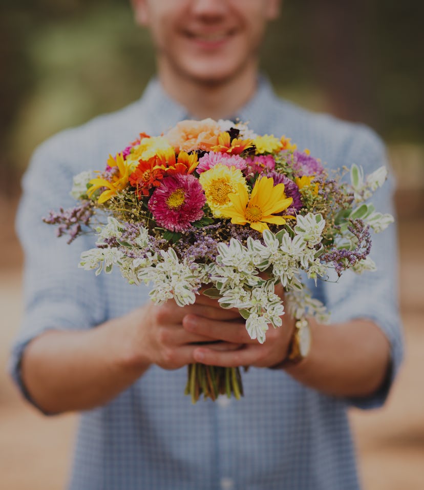 A young man is holding a beautiful bouquet of autumn flowers in his hand. The guy decided to make a ...