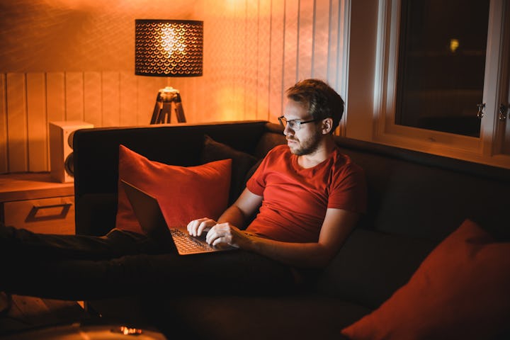 Portrait of attractive nerdy man with glasses is working late night on the computer in living room i...