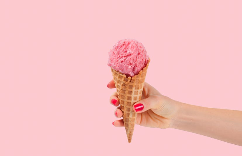 Hand holding strawberry ice cream cone on pink faded pastel color background. Strawberry ice cream i...