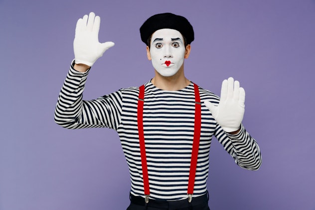 Bright young mime man with white face mask wears striped shirt beret looking camera hands raised as ...