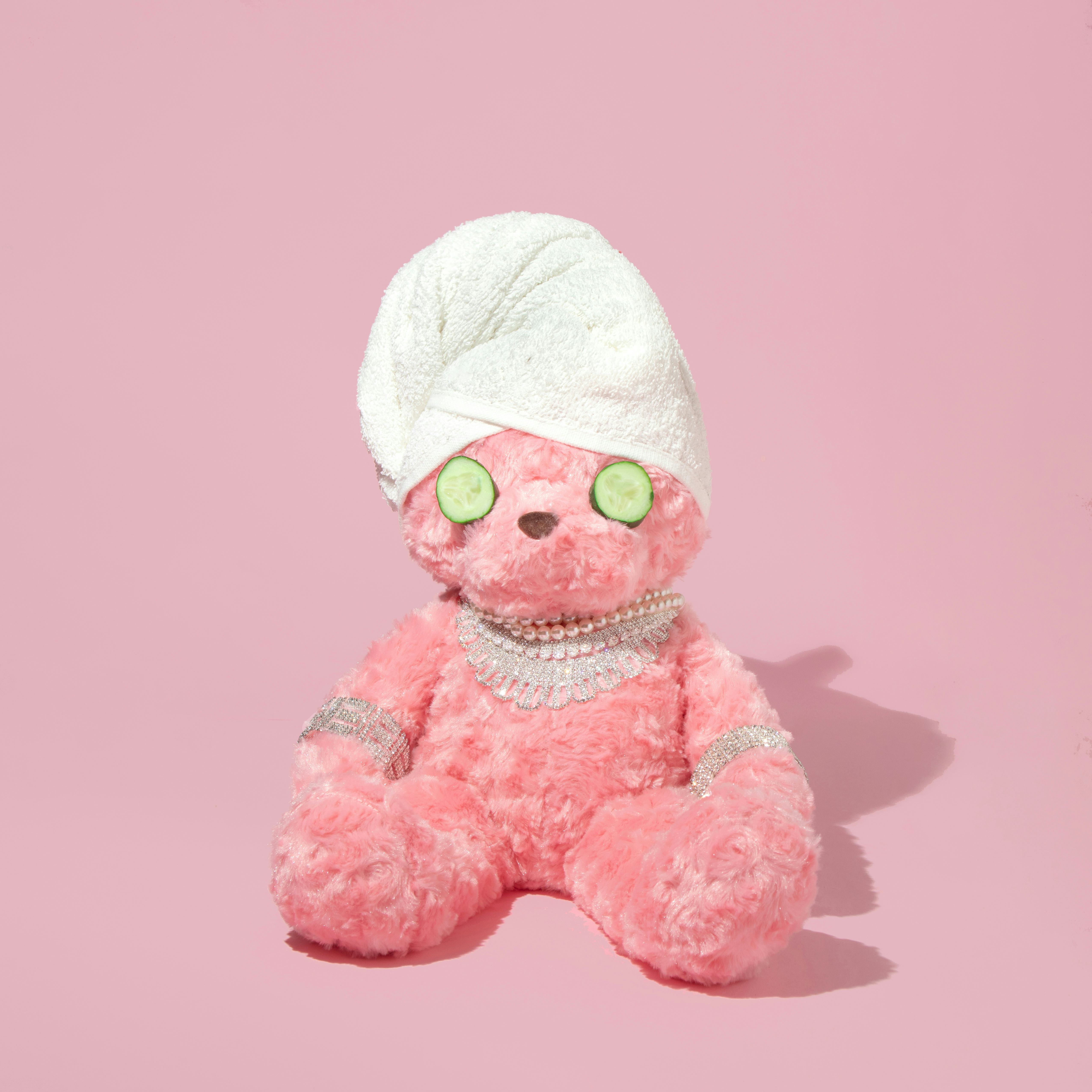 Creative layout with pink teddy bear with towel turban, cucumber slices and luxury jewelry on pastel...