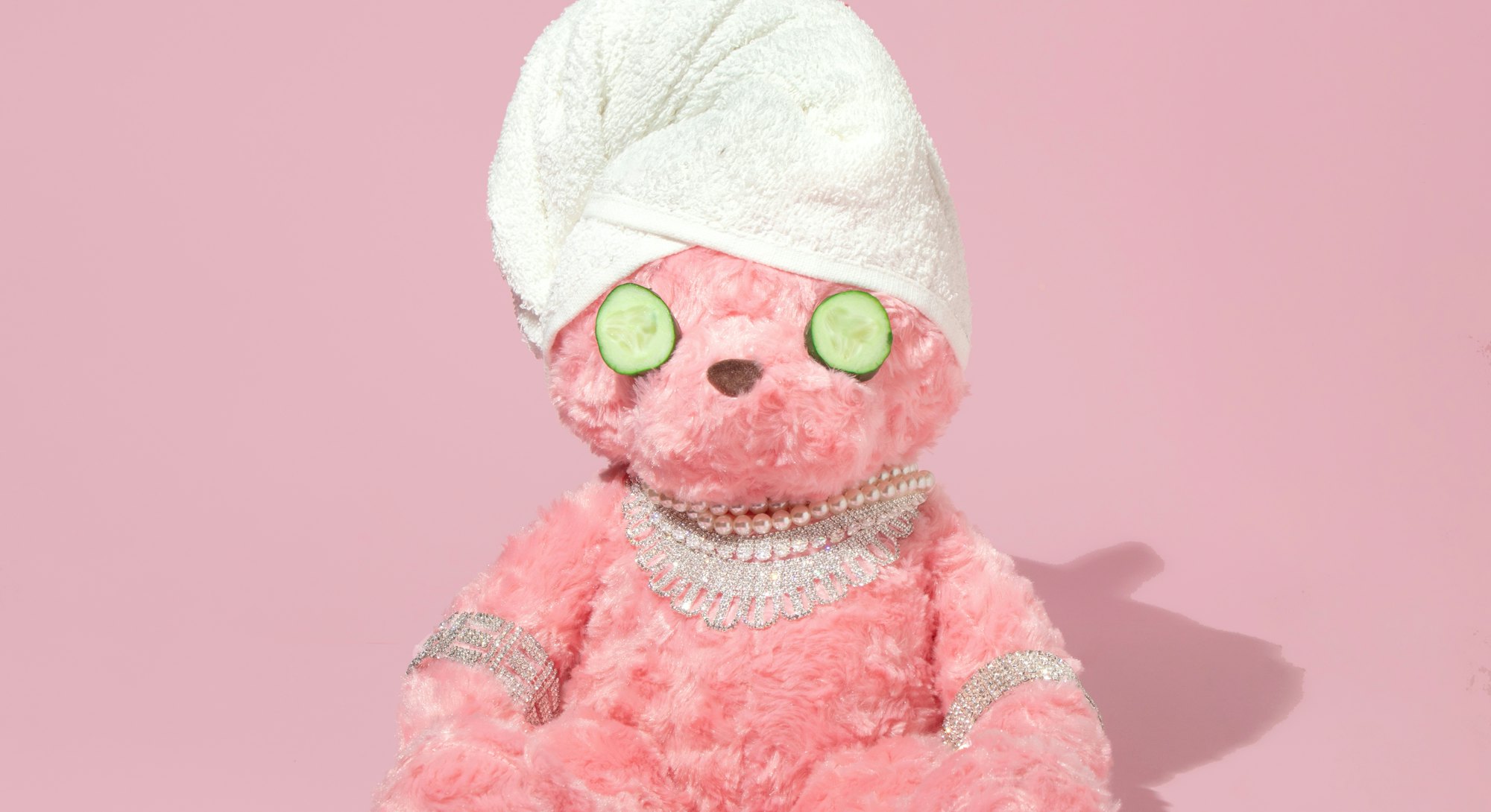 Creative layout with pink teddy bear with towel turban, cucumber slices and luxury jewelry on pastel...