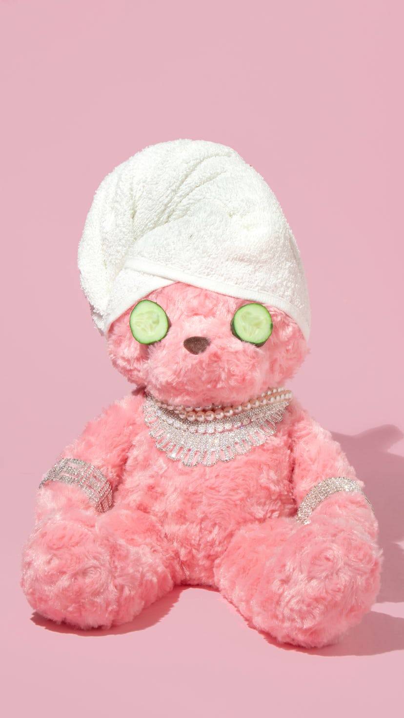 Creative layout with pink teddy bear with towel turban, cucumber slices and luxury jewelry on pastel...