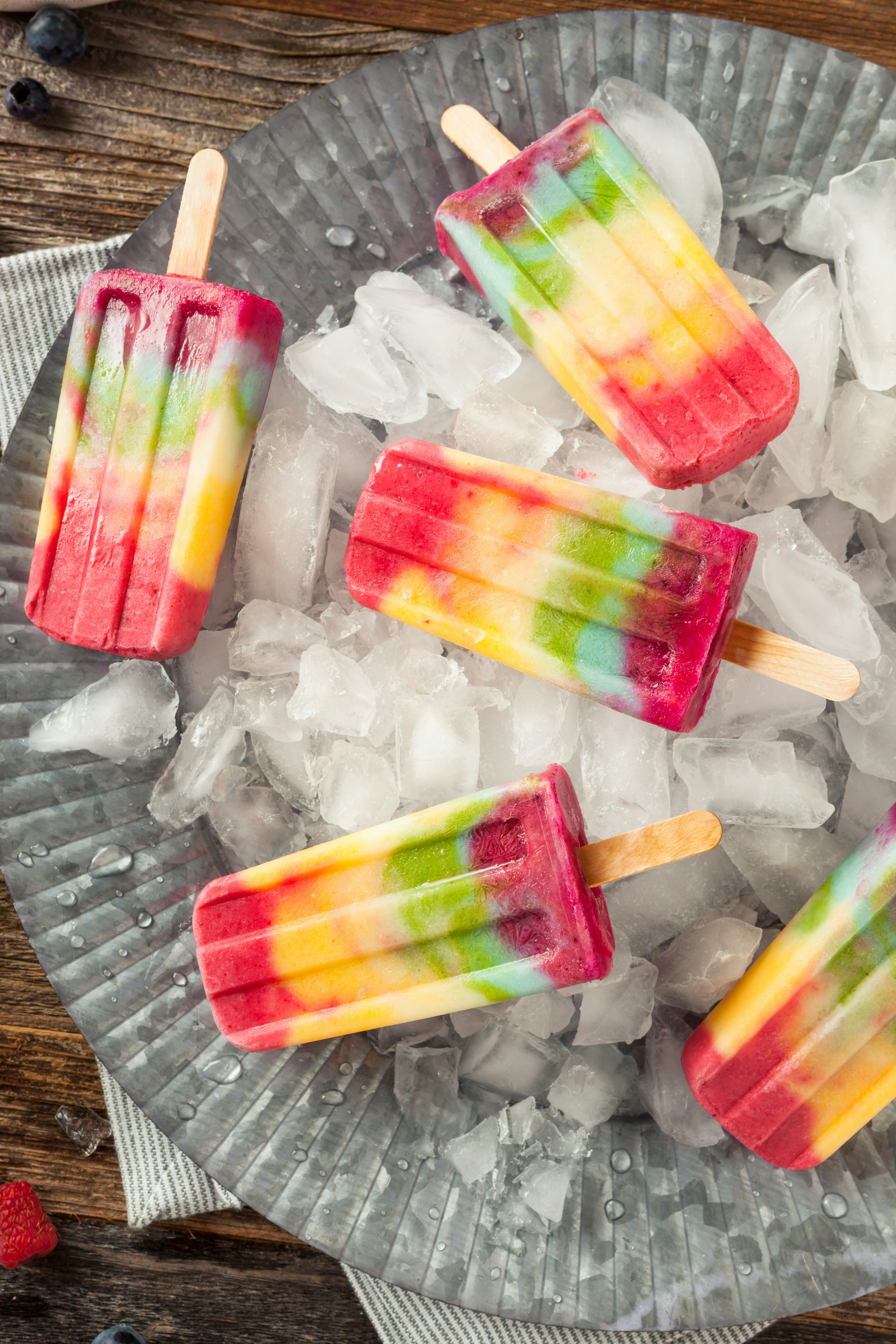 Homemade rainbow popsicles scattered on a tray of ice for summer popsicle inspiration.