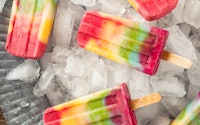 Homemade rainbow popsicles scattered on a tray of ice for summer popsicle inspiration.