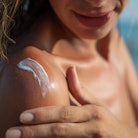 Close up of smiling young woman is applying a sunscreen or sun tanning lotion on a shoulder to take ...