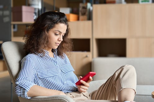 Hispanic young woman holding smartphone using phone in modern creative office. Latin girl student lo...