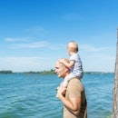 Happy father and cute kid sitting on shoulders looking on blue sea.