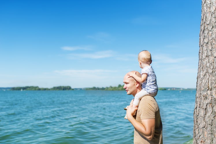 Happy father and cute kid sitting on shoulders looking on blue sea.