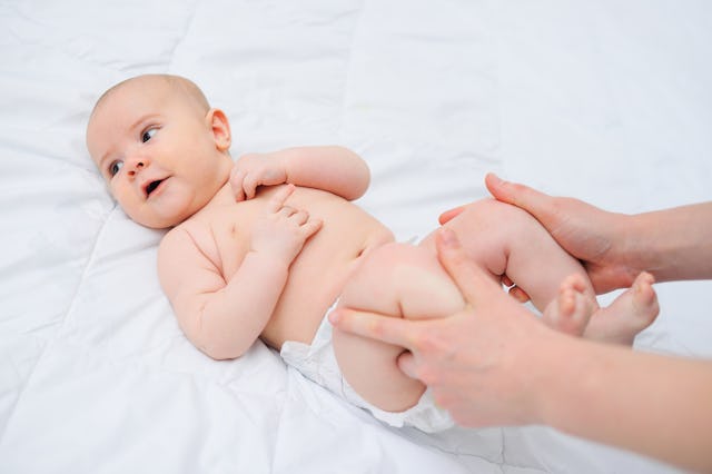 mom's hands hold the baby's legs at his tummy. Massage a newborn baby against bloating and colic.