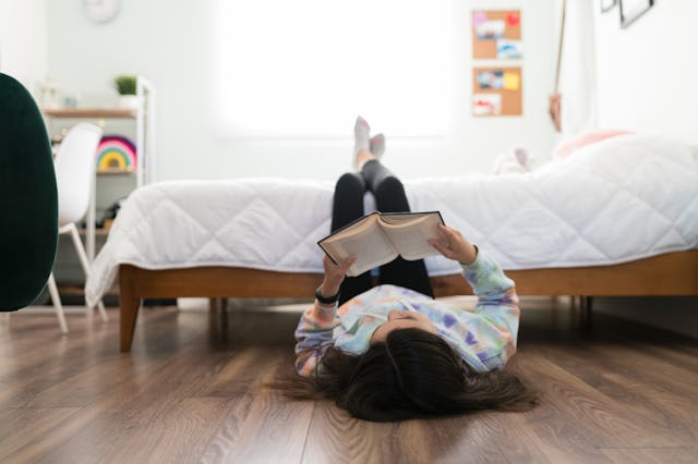Studious adolescent girl reading a book and enjoying a story in her bedroom. Young teenage girl lyin...