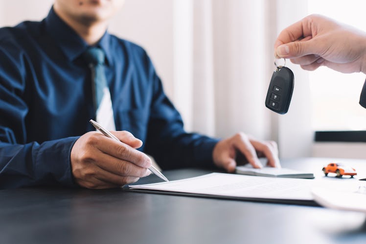 A man signs a car contract and a car dealer hands him keys over the desk